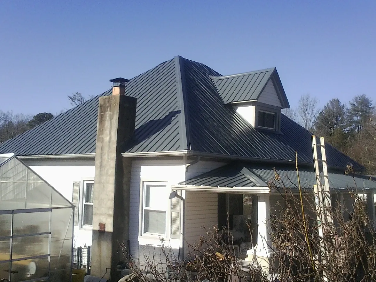 Dark blue standing seam metal roof on a white farmhouse with dormer — Slate & Tile Roof Repair by Roofing Brothers in Rush Center
