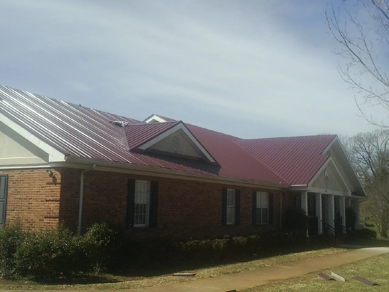 Red metal roof with gabled entries on a long brick building, from a Hail Damage Roof Repair job in Rush Center