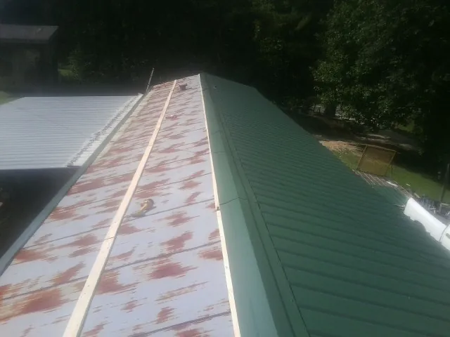 Old rusted panels beside newly installed green metal roofing — Wind Damage Roof Repair by Roofing Brothers in Rush Center