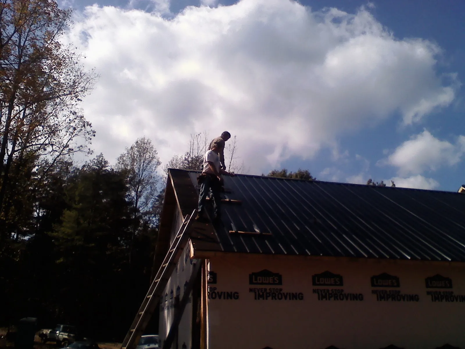 Roofer fastening dark metal panels high against a cloudy sky, from a Roof Inspection job in Rush Center