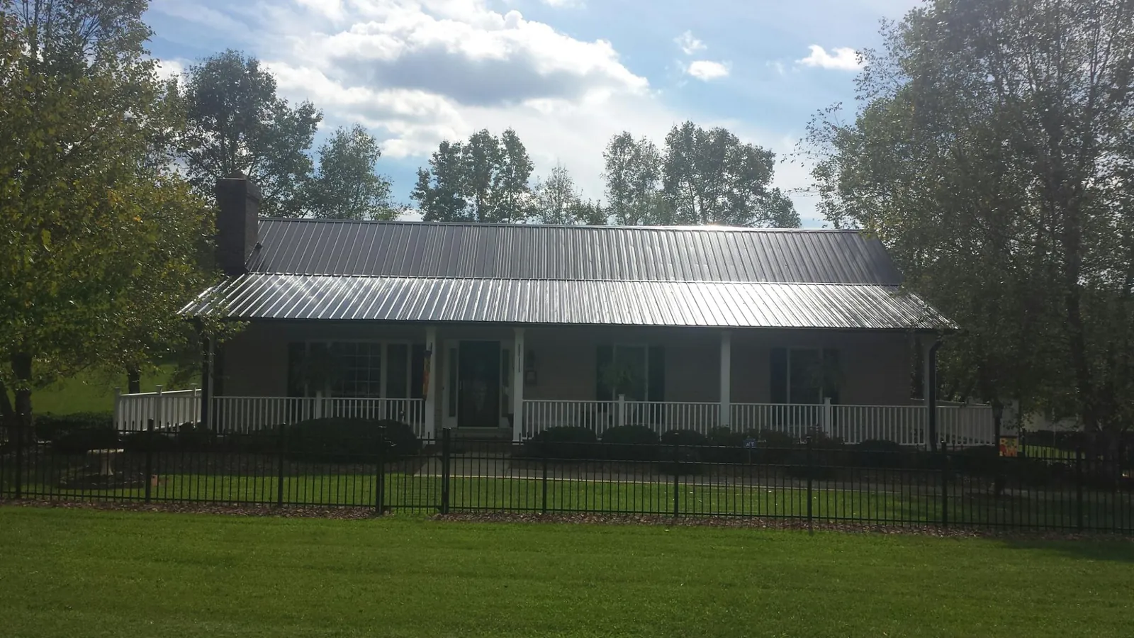 Gray metal roof on a brick ranch with a full width front porch — Gutter Guard Installation work by our crew in Rush Center