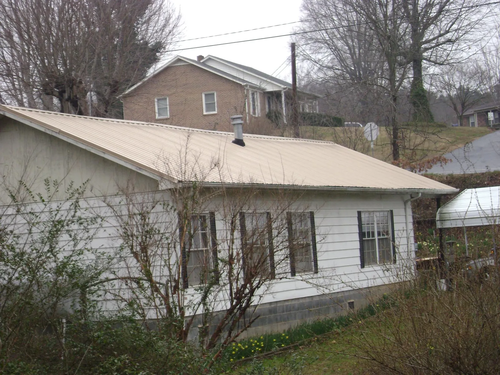 Tan metal roof on a white sided house set into a hillside — Commercial Roofing by Roofing Brothers in Rush Center