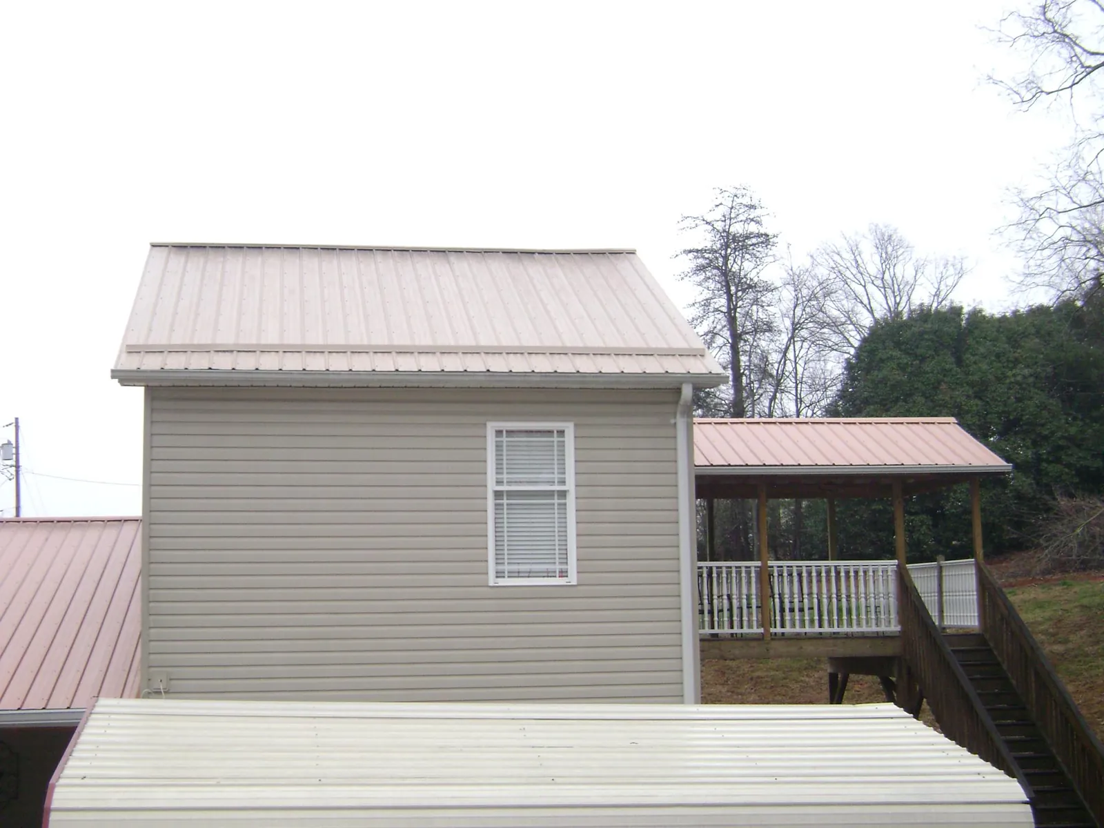 Tan metal roofs on a two story addition and attached porch, from a Roof Replacement job in Rush Center